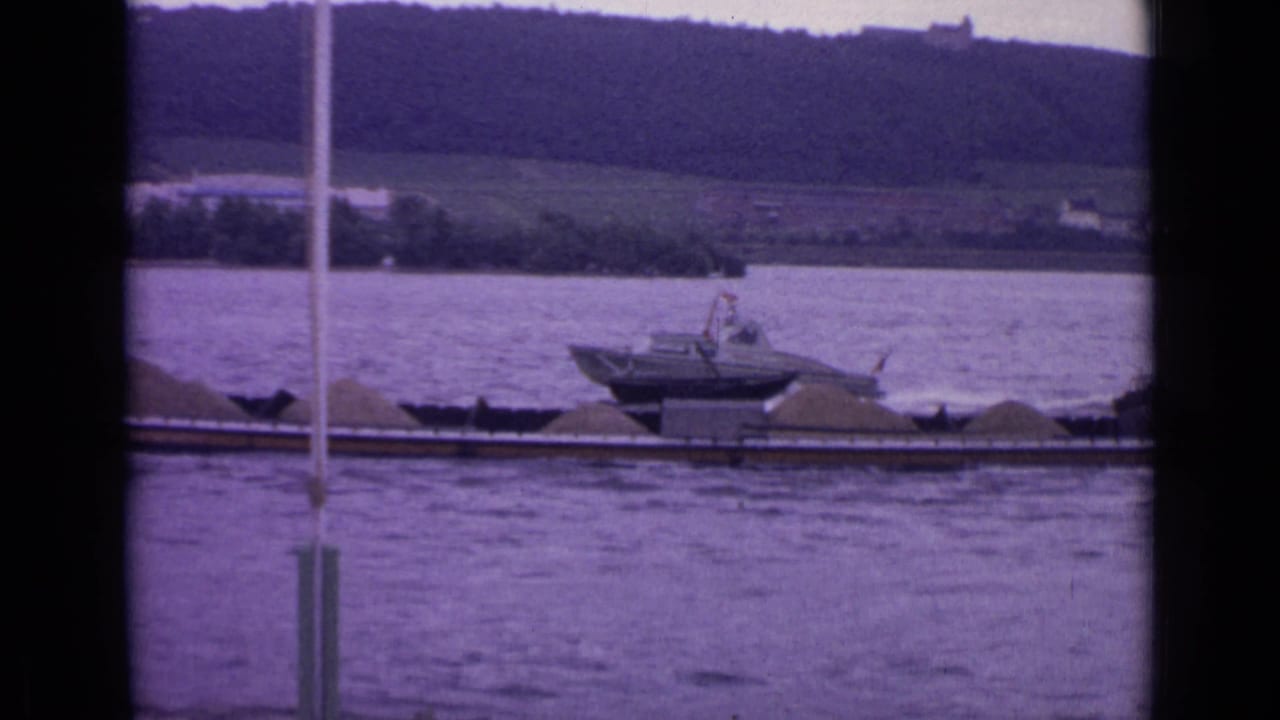 Small motorboat near a loaded barge on a river with hillside in the background.