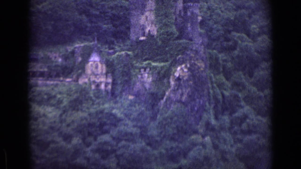 German 1962 home-movie frame of cliff ruins and a chapel-like structure viewed through soft, grainy 8mm color footage.
