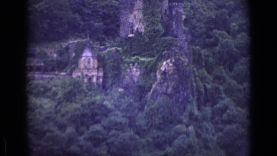 German 1962 home-movie frame of cliff ruins and a chapel-like structure viewed through soft, grainy 8mm color footage.