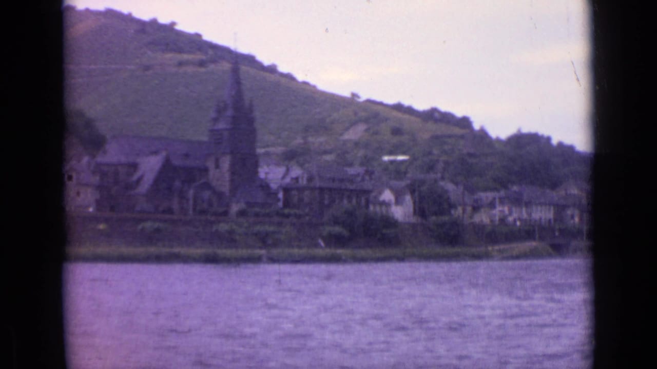 Riverside town with church spire and hillside vineyards across the water.