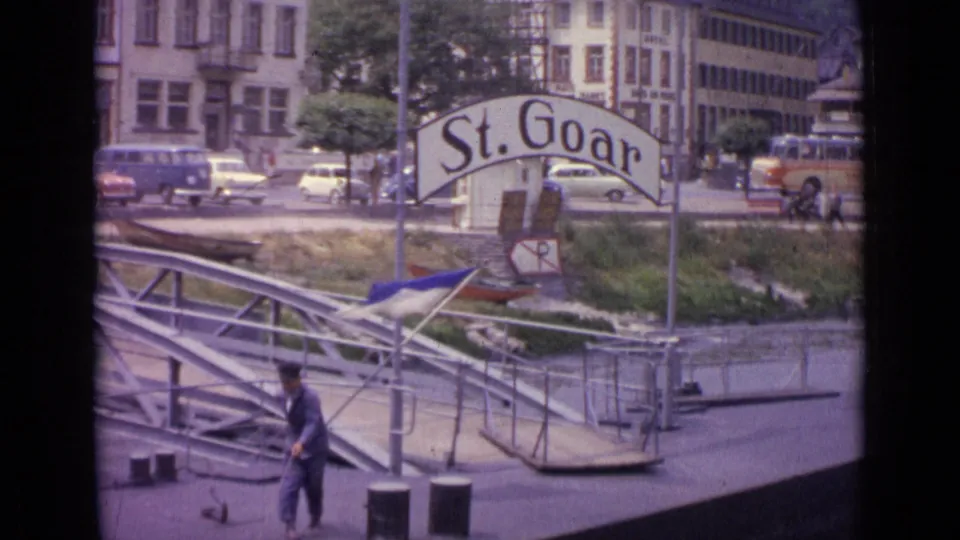 1962 St. Goar pier view with the sign, metal gangway, moored small boat, traffic, and a man moving near the lower foreground.