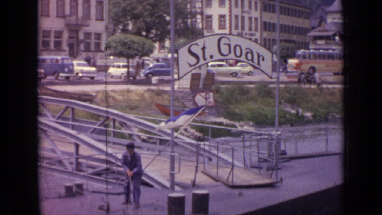 Man stands on the dock with a rope near the St. Goar sign and riverfront traffic.