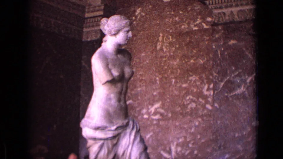 1962 Germany 8mm frame showing a classical armless female statue, likely in a museum interior, against a mottled wall surface.