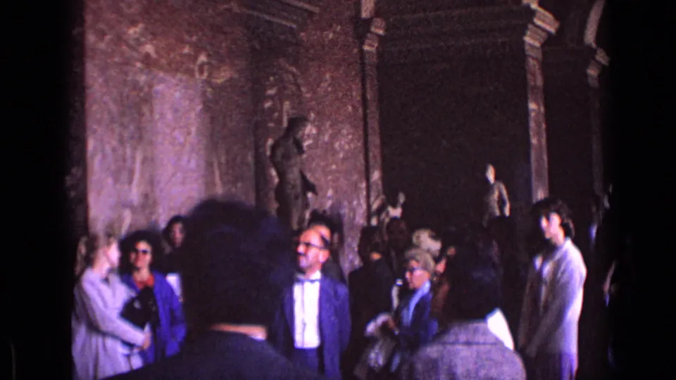 1962 Germany museum visitors stand beneath ornate walls near classical statues, with a suited man and bow tie near the center.