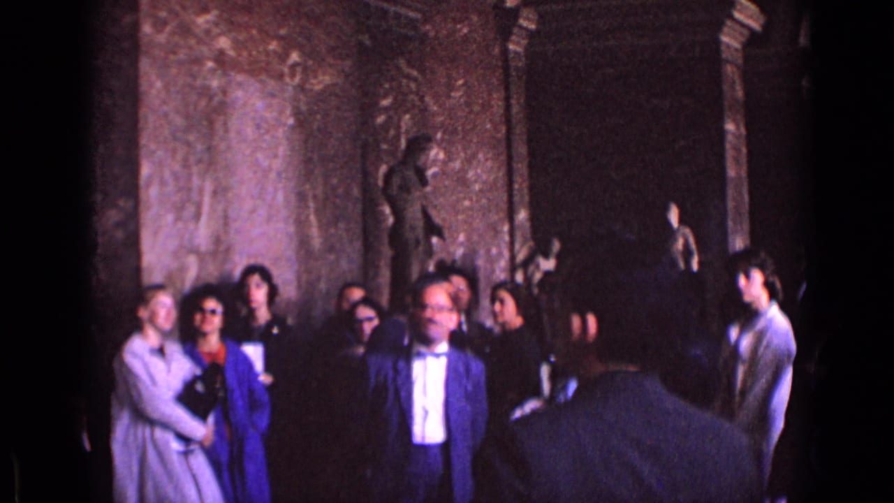 In a German museum gallery, adults in 1960s dress stand among columns and classical statues while another visitor is seen from behind.