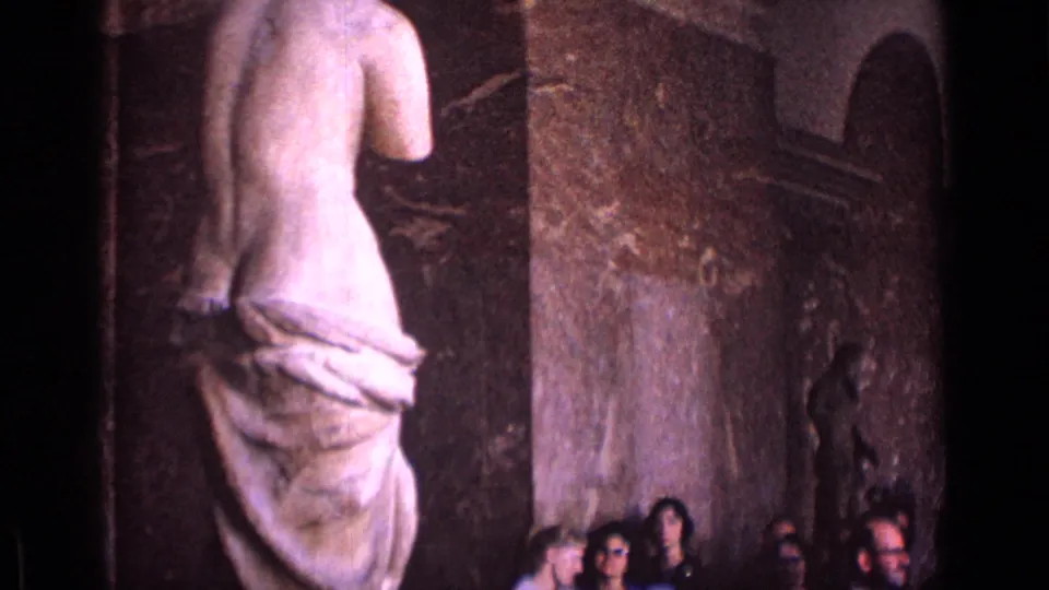 A classical marble figure dominates the foreground in a German museum gallery, with visitors partly visible near the textured wall.