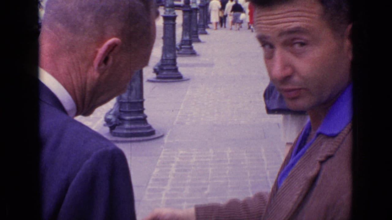 A close 1962 home-movie frame shows a man in a brown jacket glancing at the camera while an older man faces the street.