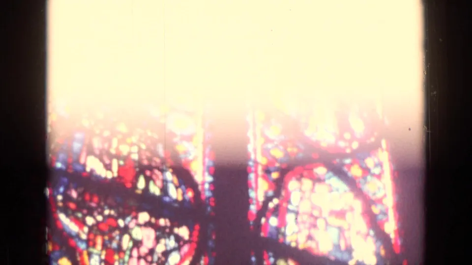 Overexposed 8mm view of colorful stained glass, with red and blue sections visible below bright window glare.