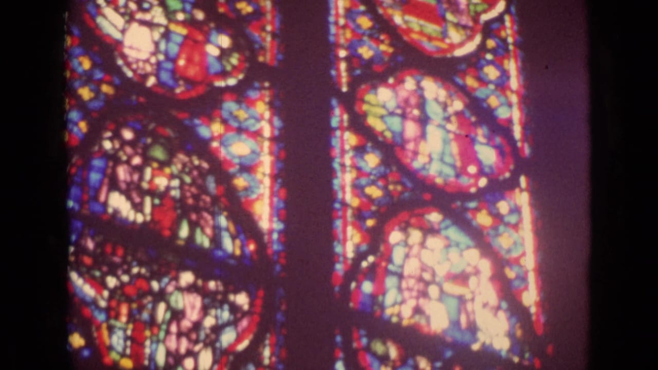 1962 Germany 8mm frame showing tall stained-glass panels glowing inside a dark church interior.