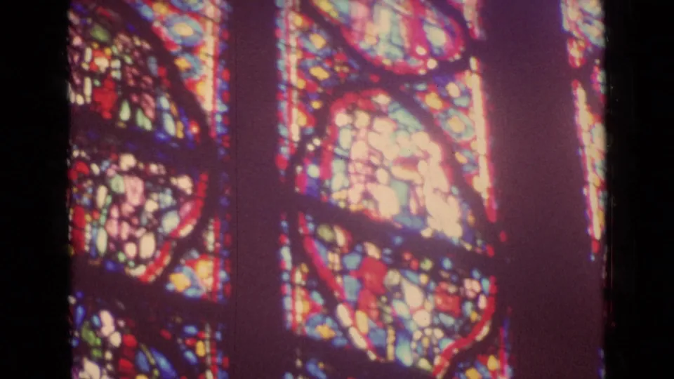 Visitor-shot 8mm view of detailed stained glass inside a German church, with bright colored medallions and dark framing.