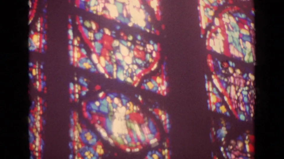 Soft handheld 8mm frame of colorful church stained glass in Germany, with bright figure panels and visible film texture.