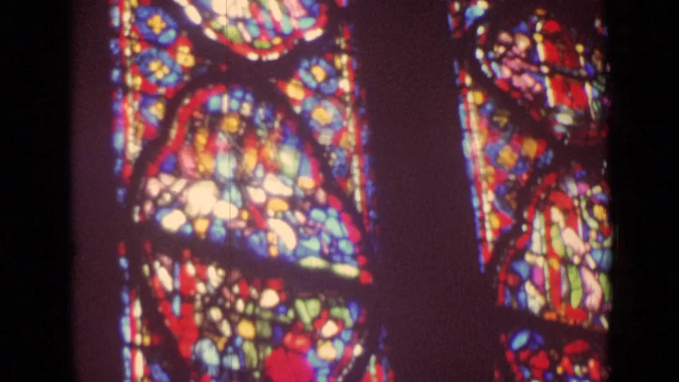 1962 German 8mm frame showing glowing abstract stained glass inside a church, partially divided by a dark column or frame.