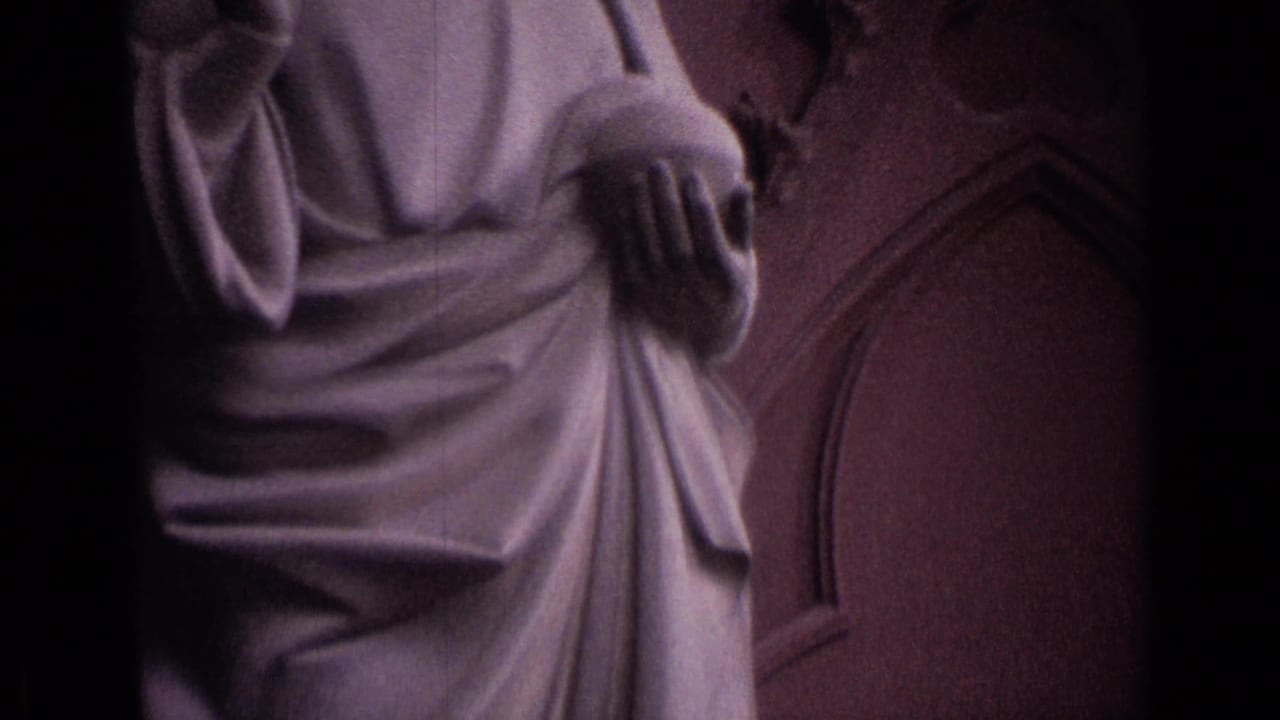 Upper portion of a robed stone statue near a stained glass window.
