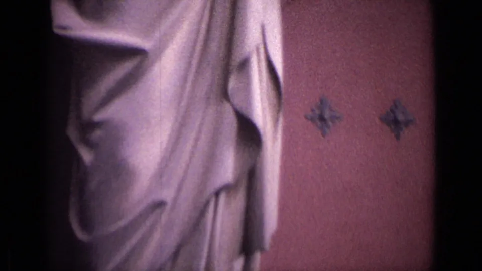 Close view of the lower robes of a stone religious statue against a pink-toned church wall in the 1962 German 8mm footage.