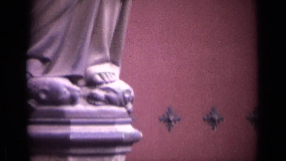 1962 German church frame showing the statue's feet on an ornate pedestal, with pink wall surfaces and small decorative motifs behind it.