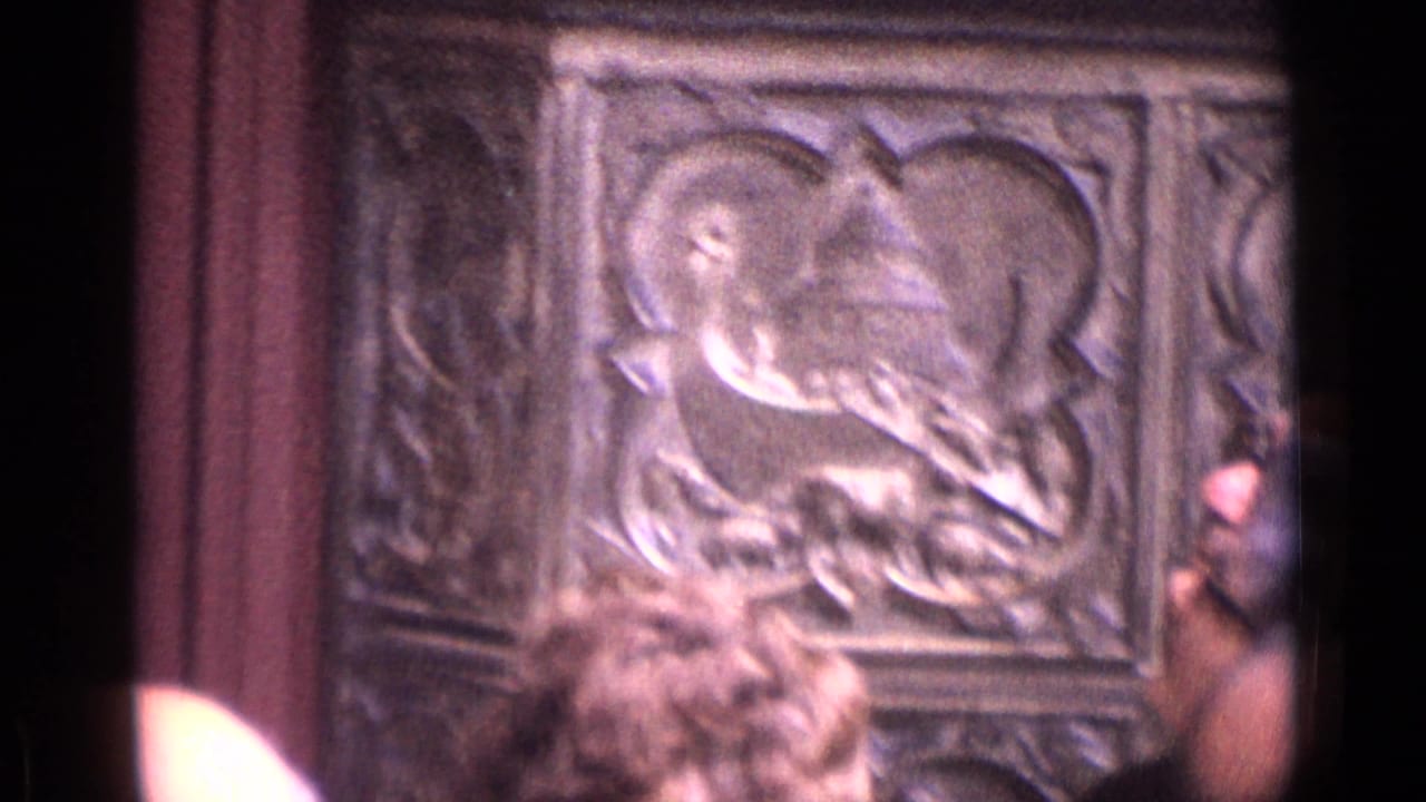 Carved religious-looking relief panel in a German cathedral interior, partly obscured by tourists in the foreground.