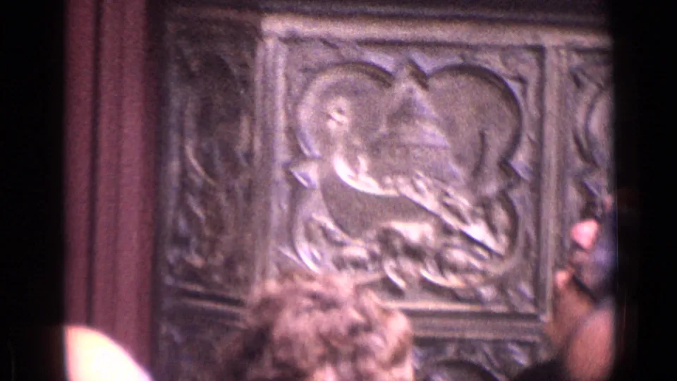 Carved religious-looking relief panel in a German cathedral interior, partly obscured by tourists in the foreground.