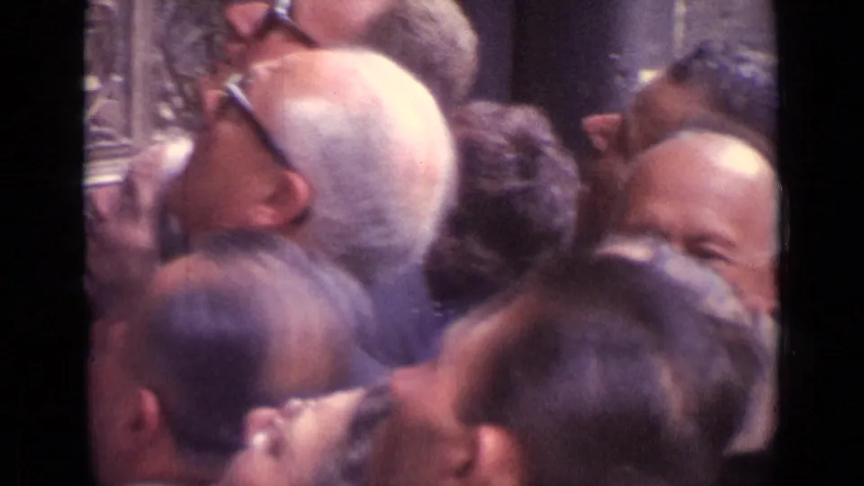 Close crowd of 1962 Germany cathedral visitors looking upward toward unseen architectural details in a dim interior.