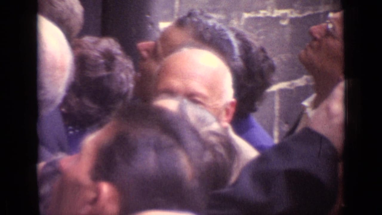 In Germany 1962 home-movie footage, adults stand closely together indoors and look upward in dim light.