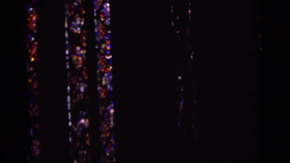 A dim 8mm view of vertical stained glass panels glows with red, blue, and purple color in the interior.