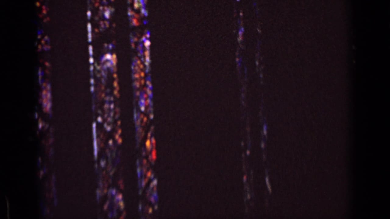 Dim 8mm church interior in Germany, 1962, with narrow stained glass windows partly visible through dark exposure.