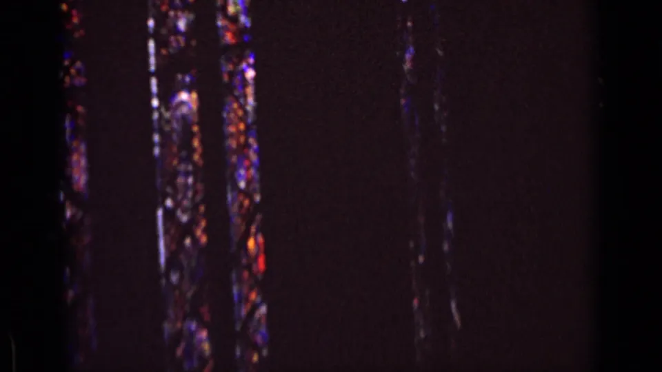 Dim 8mm church interior in Germany, 1962, with narrow stained glass windows partly visible through dark exposure.