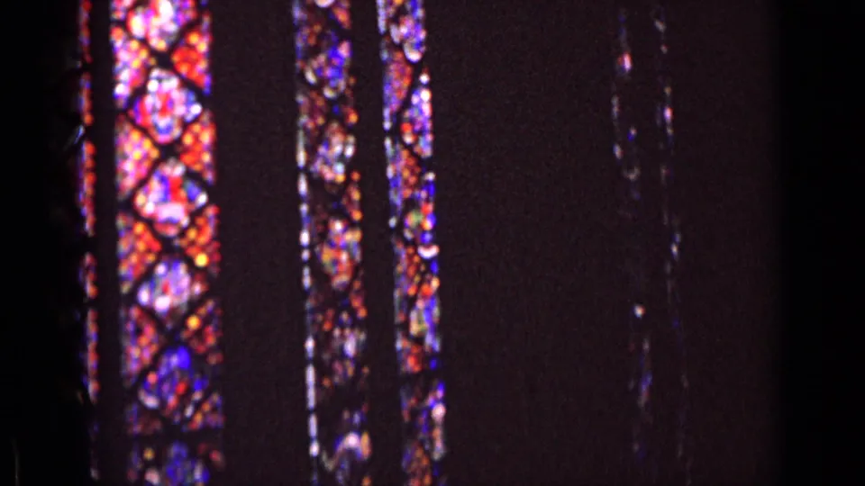 Colorful stained glass fills part of a dark 1962 Germany church frame, with reds, blues, and purples visible in soft 8mm focus.