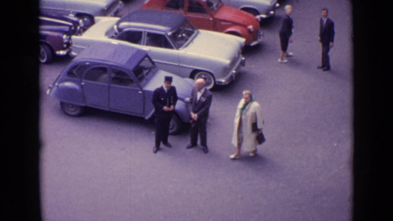 Elevated street view with parked classic cars and several adults near a blue compact car.