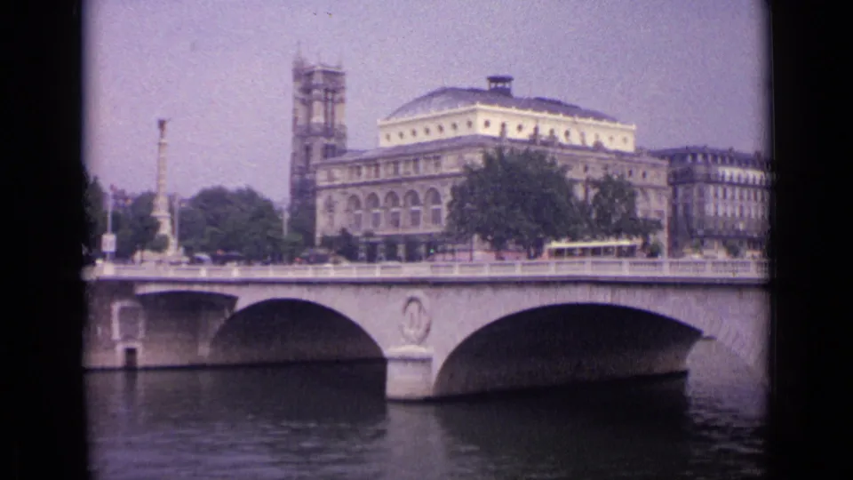 Wider 8mm view of the German city bridge scene, with river water below, a tram and cars above, and historic architecture beyond.