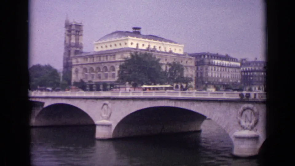 Final frame of the 1962 Germany bridge view, showing the river crossing, small pedestrians, period vehicles, and large urban buildings.