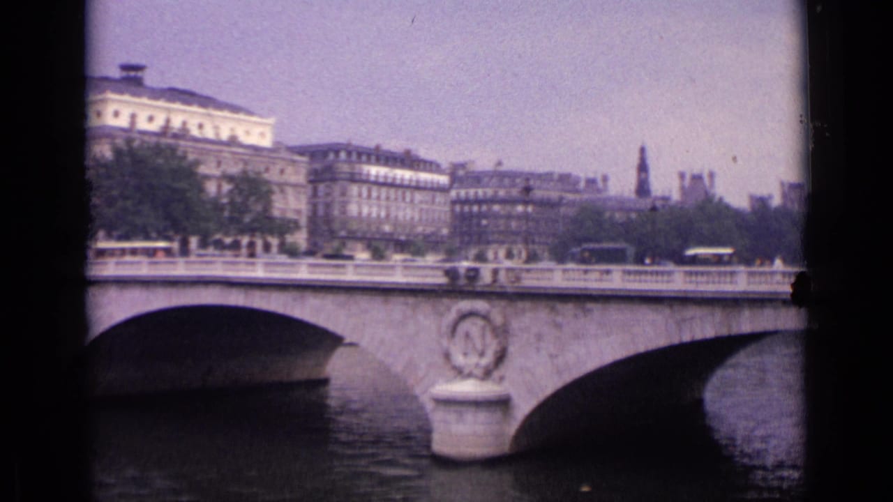 1962 German city bridge scene with cars or buses crossing, a stone arch over the river, and multi-story buildings in the background.