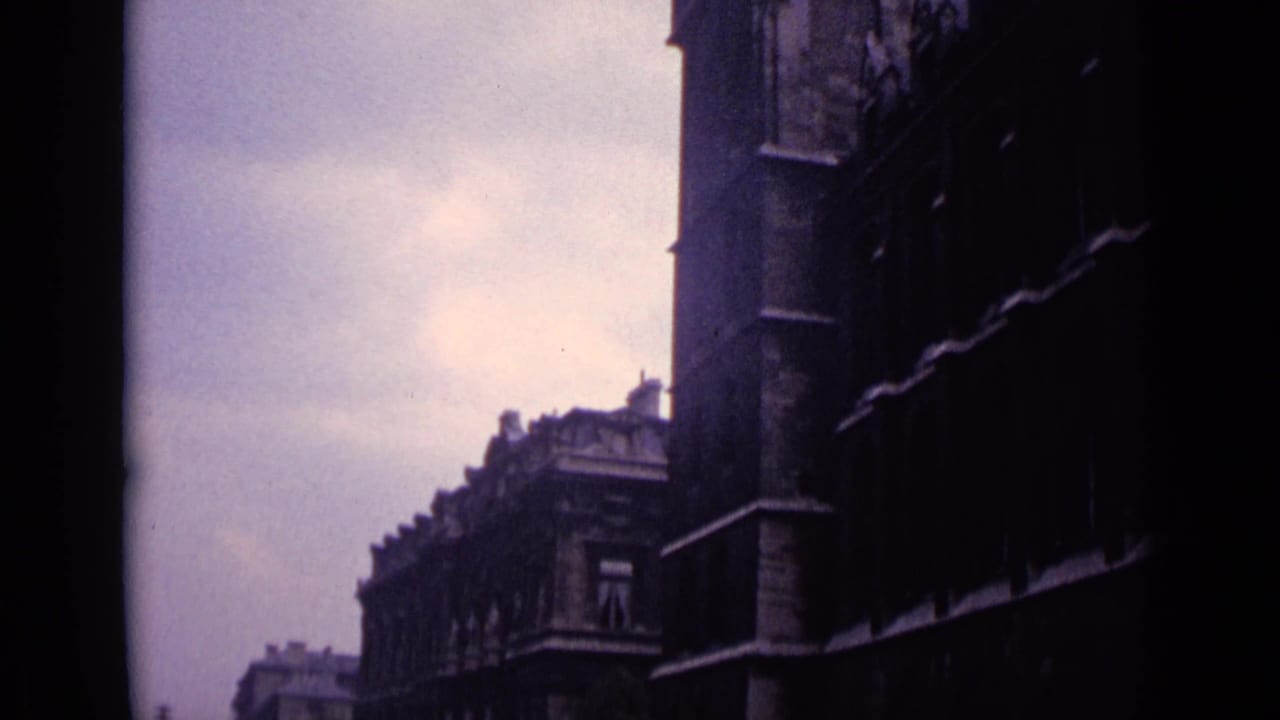 Handheld 8mm view in Germany, 1962, looking along a dark historic facade and roofline under a cloudy sky.