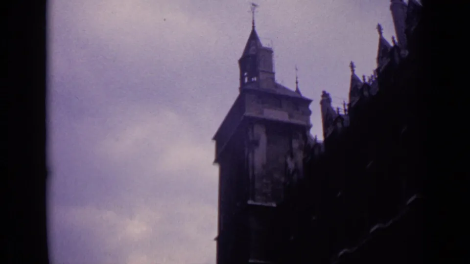 Germany 1962 8mm frame showing a church tower, steep roof, and shadowed historic facade against overcast sky.