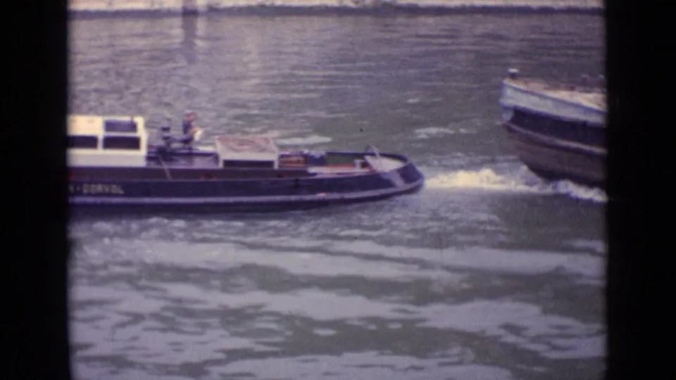 The tugboat continues across the river while another vessel appears at the right edge, with wake and grainy 8mm texture visible.