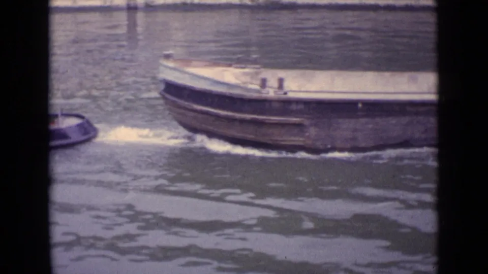 1962 Germany frame with the front of a large empty barge and part of a tugboat crossing the river view.