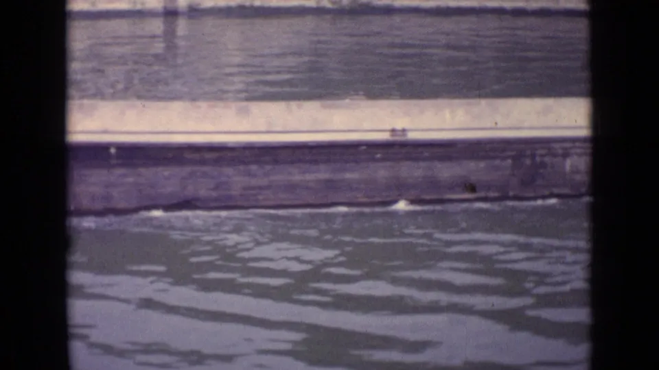 1962 Germany frame of an empty barge's side moving across the river, with water wake beneath it.