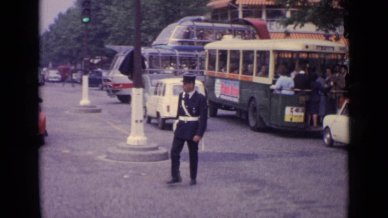 Traffic officer standing in a city street as buses and small cars move through the intersection.