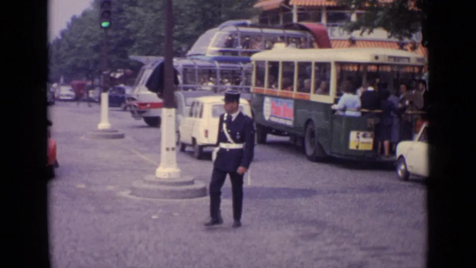 Germany 1962 8mm frame showing a uniformed traffic officer directing traffic near buses and compact cars on a city street.