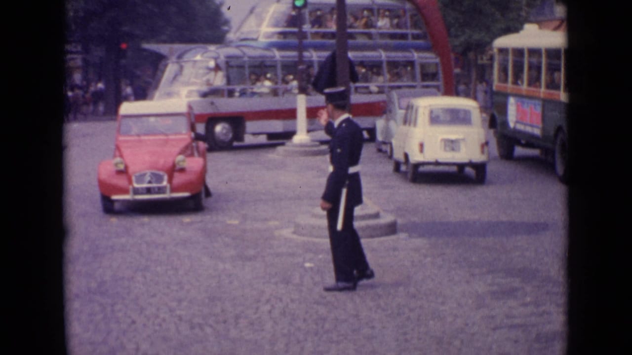Germany 1962 street frame with a traffic officer signaling near a red compact car, a small white car, and a glass-roof double-decker bus.
