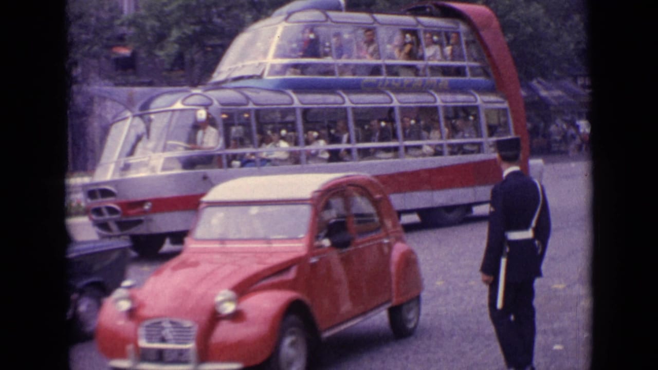 Red compact car passing a large double-decker bus while a uniformed officer stands in the road.