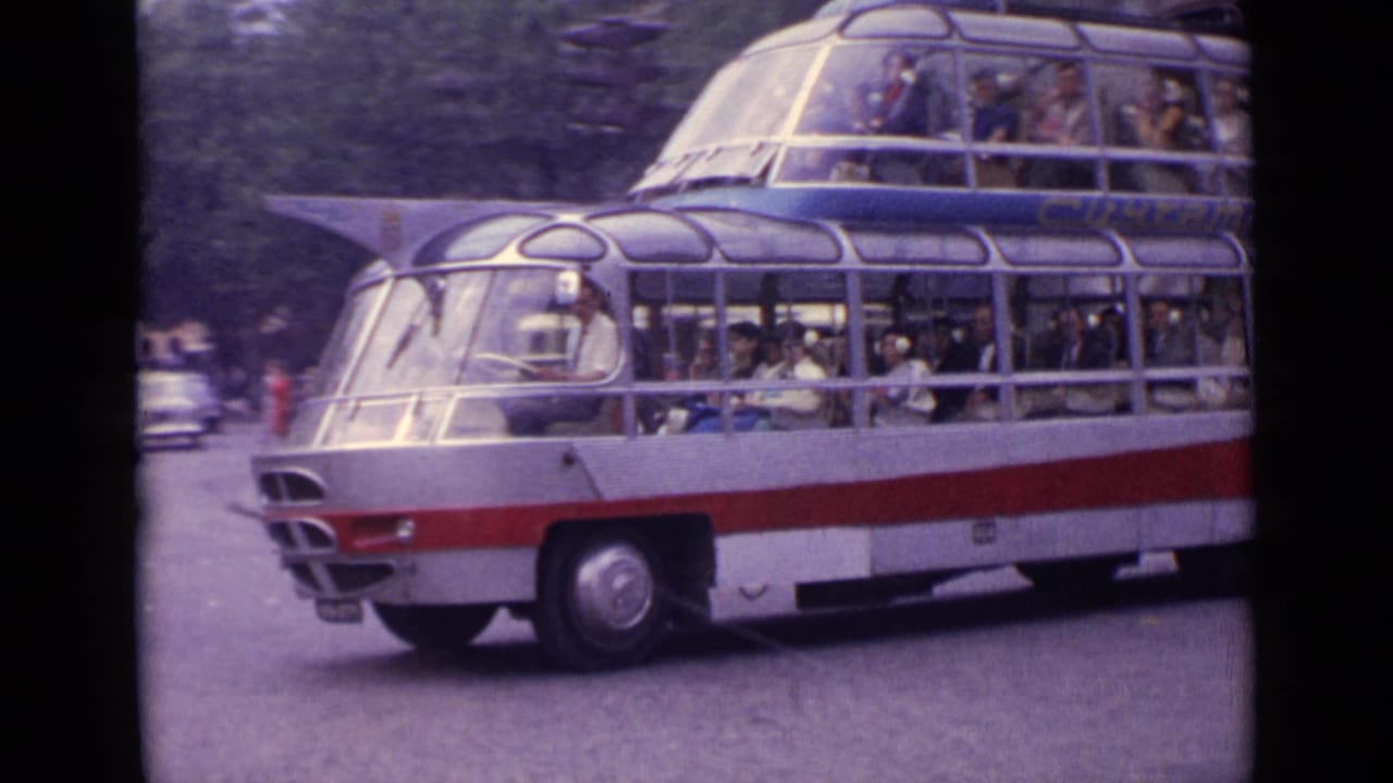 Large 1960s double-decker bus with curved glass windows travels through traffic on a German street.