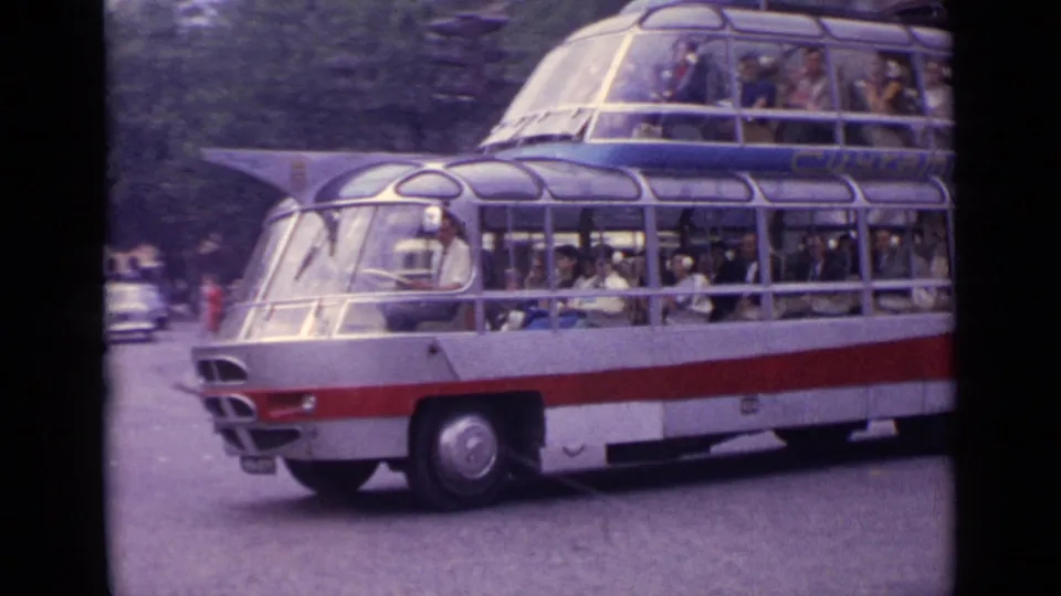 Large 1960s double-decker bus with curved glass windows travels through traffic on a German street.