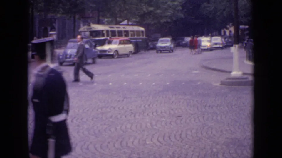 1962 Germany home-movie frame showing a cobbled city street with pedestrians, period cars, a bus, and a lamp post before the church-detail views.
