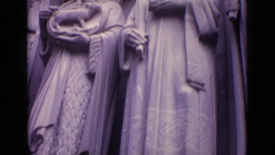 1962 Germany 8mm frame showing robed stone figures on a historic building, including one figure holding a cross-like object.