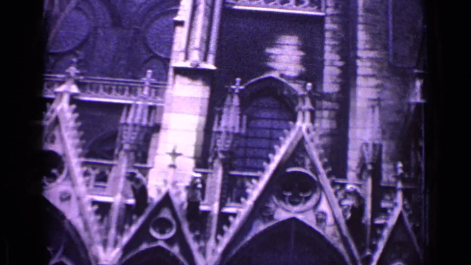 Visitor-shot 8mm view of a German Gothic church exterior, with steep gables, carved stone trim, arched windows, and soft purple film cast.