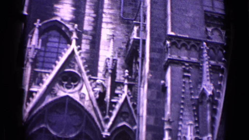 1962 home-movie frame of a Gothic church exterior in Germany, showing a large pointed gable, circular tracery, stone figures, and adjacent facade detail.