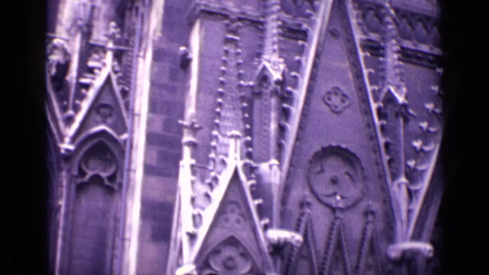 Purple-tinted 8mm frame from Germany showing Gothic church facade details, including pointed stone forms, circular ornament, narrow arches, and roof panels.