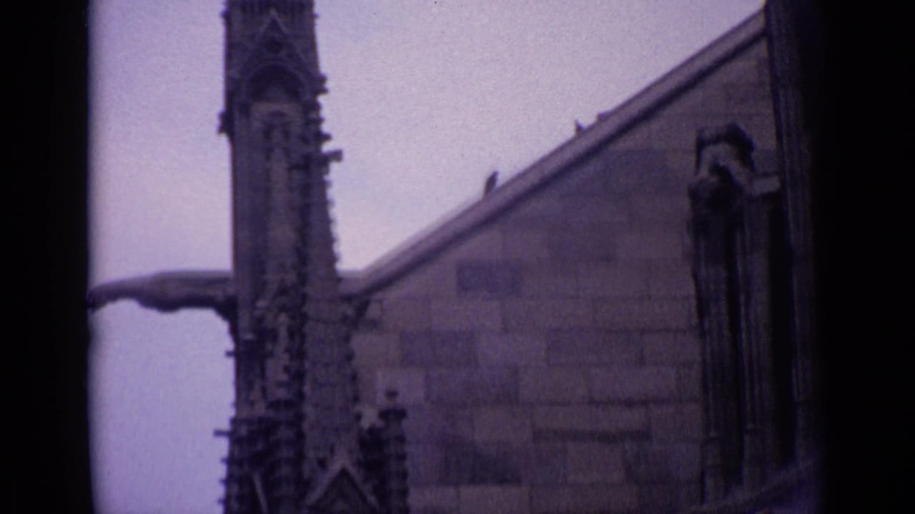Close view of church stonework with a spire, roofline, and projecting gargoyle-like spout.