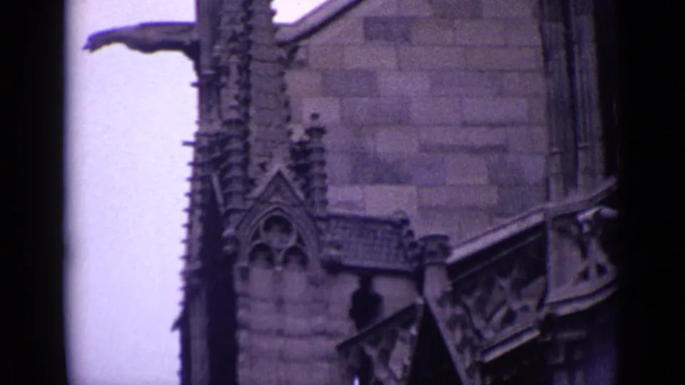 1962 Germany 8mm frame of a Gothic-style church exterior with decorative stonework, roofline detail, and shadowed arched opening.