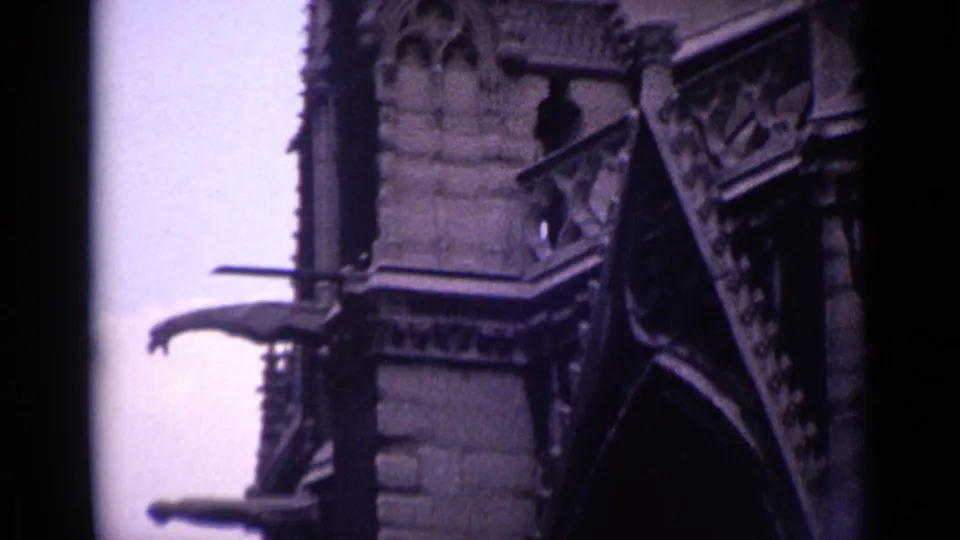 1962 Germany 8mm frame showing church facade ornament, roof edging, and multiple gargoyle-like water spouts against pale sky.